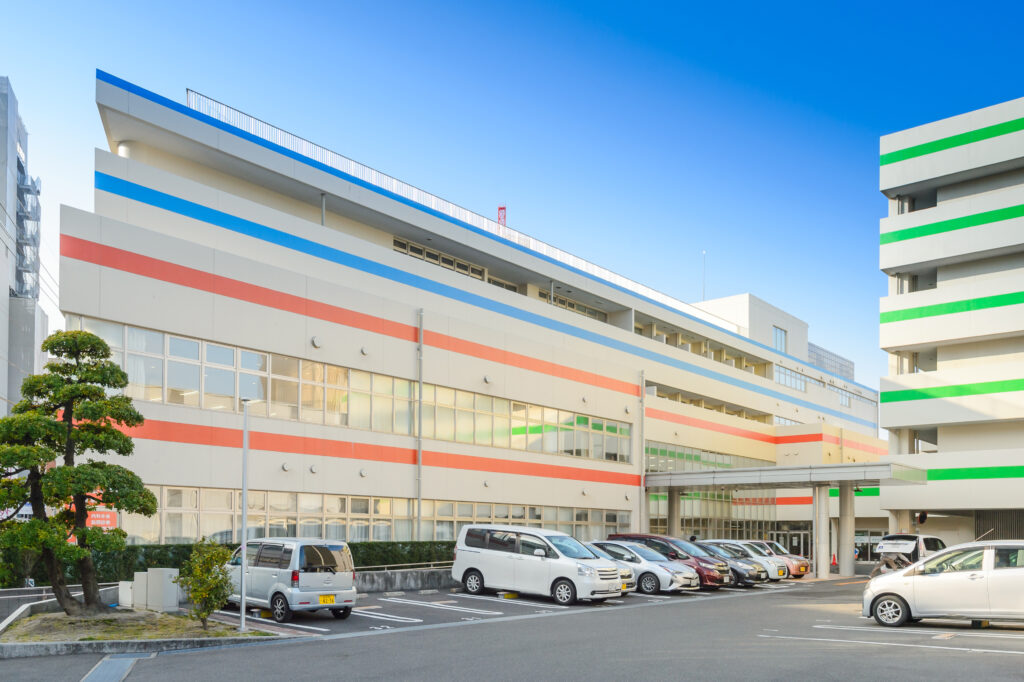 カラフルな装飾が施された介護施設の建物外観。駐車場と緑の樹木が見える。